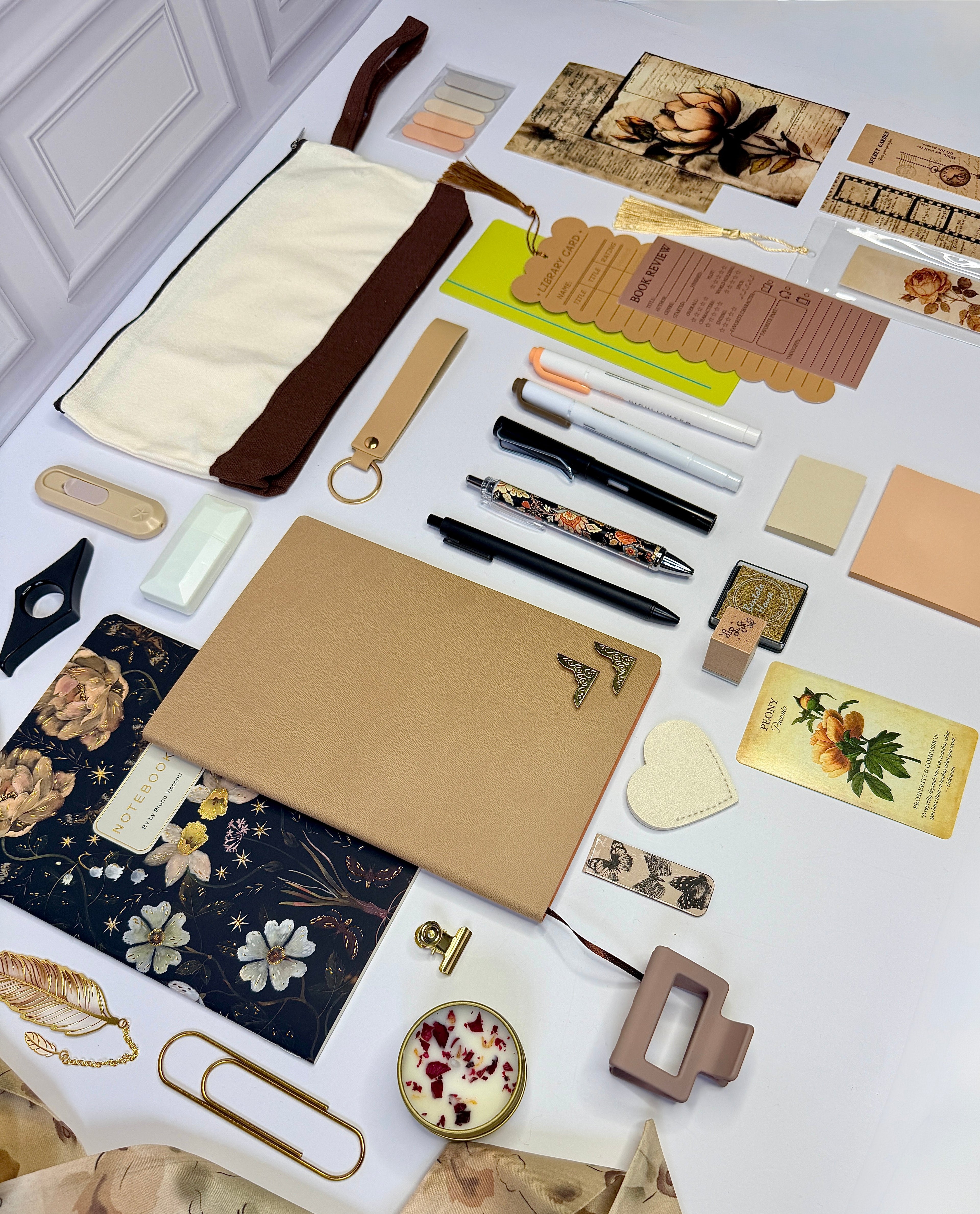 Collection of stationery items including notebooks, pens, and decorative elements on a white surface.