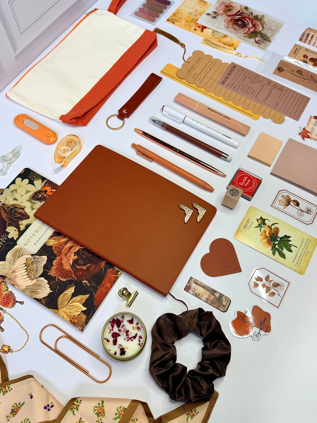 Collection of stationery items including notebooks, pens, and decorative elements on a white surface.