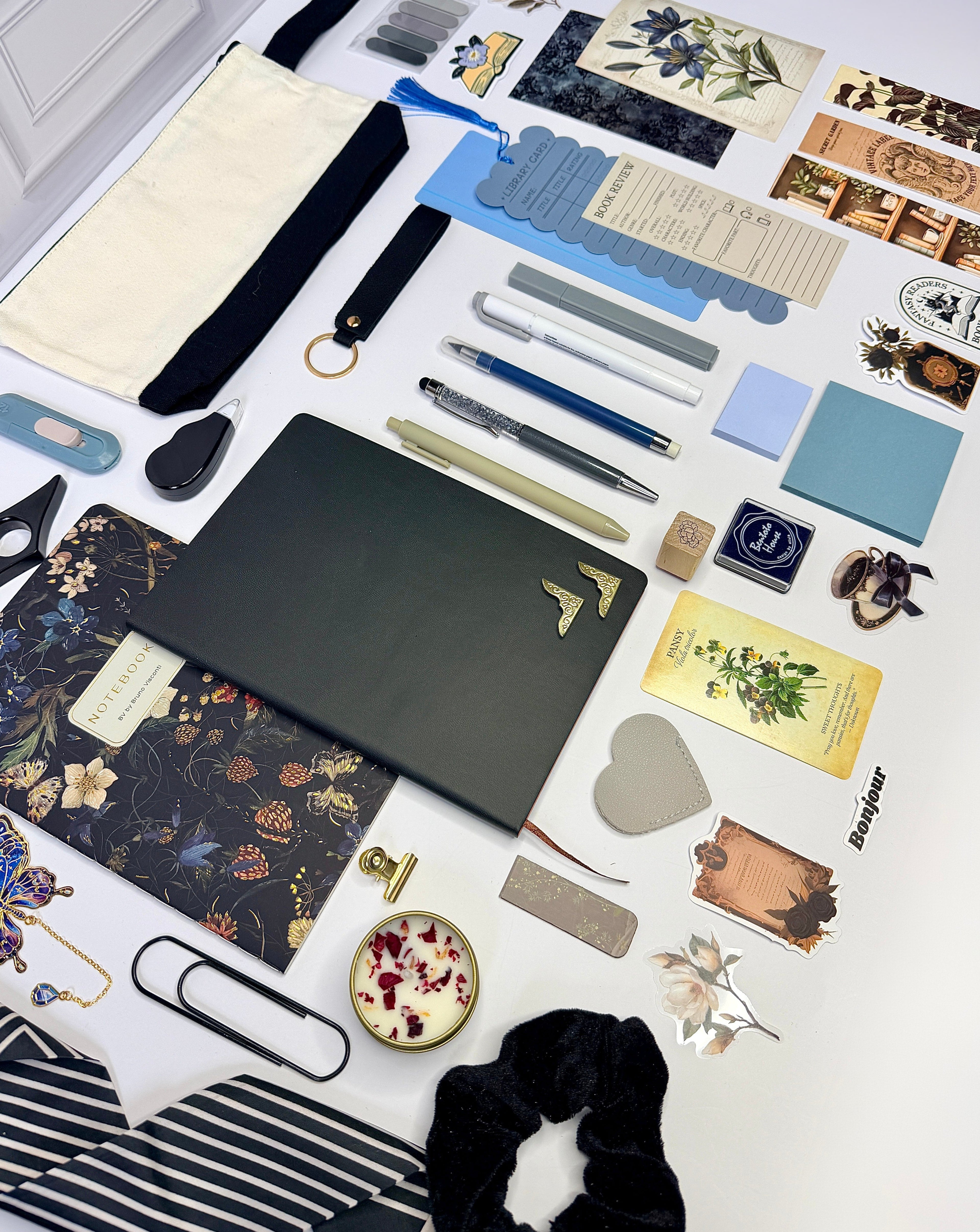Collection of stationery items including notebooks, pens, and decorative elements on a white surface.